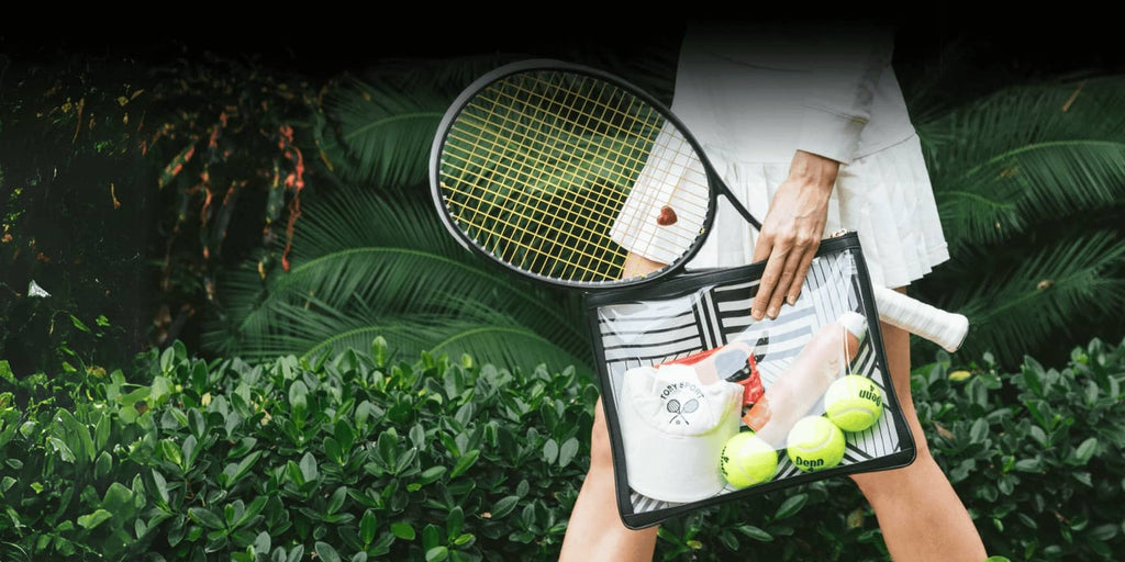 A women carrying a clear black bag with tennis balls, sunscreen and a hat. She has a tennis skirt on and holding a tennis racquet